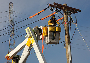 Utility worker in a bucket making repairs to a wooden utility pole