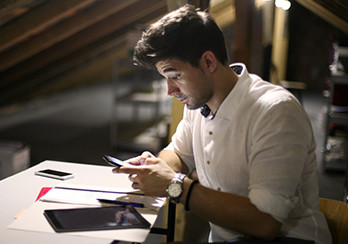 Man sitting at a table, tablet on the table, holding and looking at a smartphone