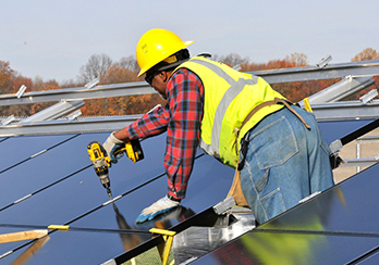 Worker in a hard hat using a tool to install a solar panel