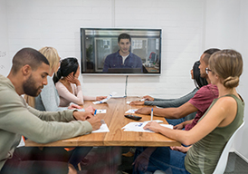 Boardroom with people sitting at a table watching a video