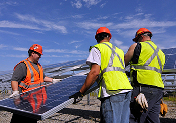 Three workers in hard hats and safety vests installing solar panels