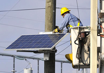 Worker in elevated lift bucket installing solar panel onto a utility pole