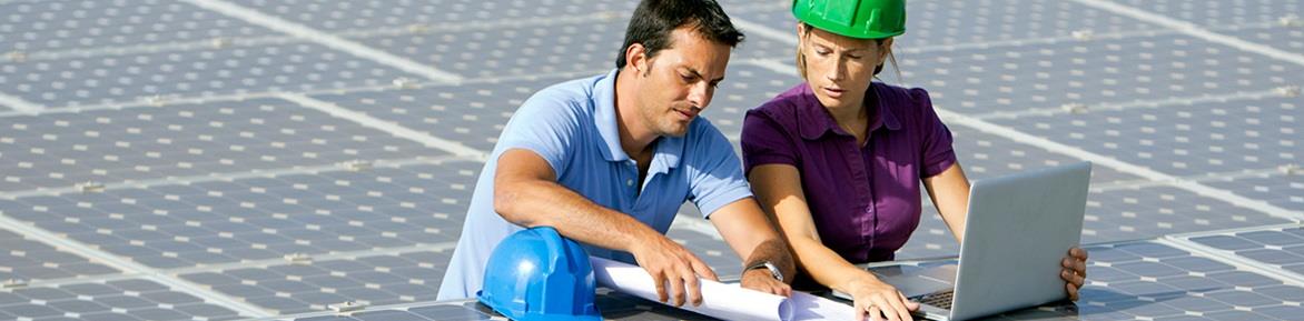 Two workers standing in the middle of a field of solar panels looking at a laptop