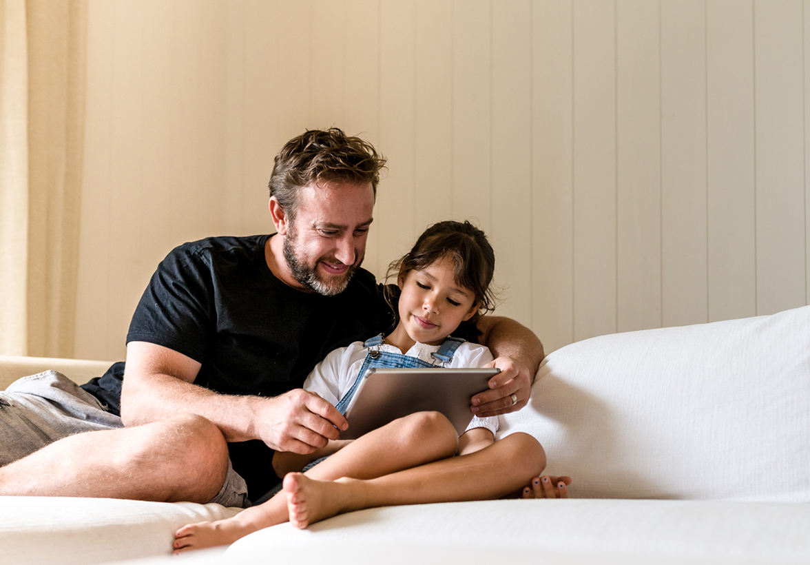 Father and daughter curled up on coach looking at a tablet
