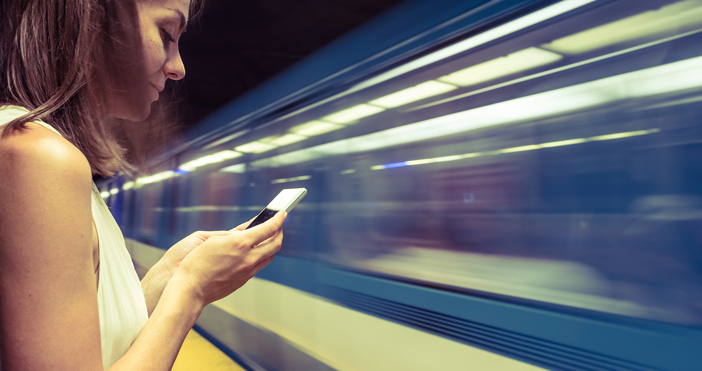 Woman with mobile fan, while train rushes past her.