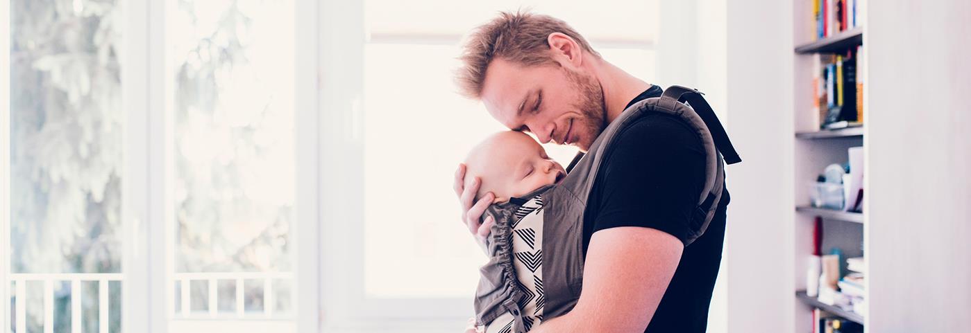 Content young father standing in family room holding a sleeping baby