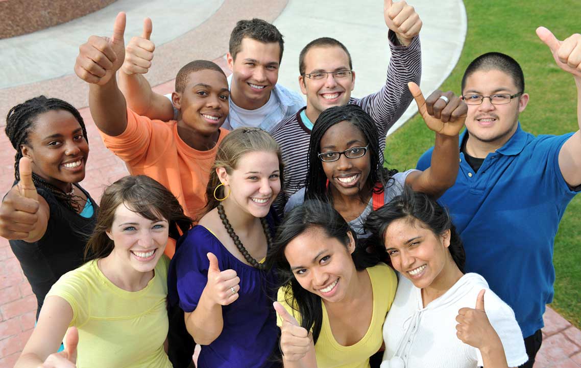 a crowd of men and women smiling for camera and giving thumbs-up
