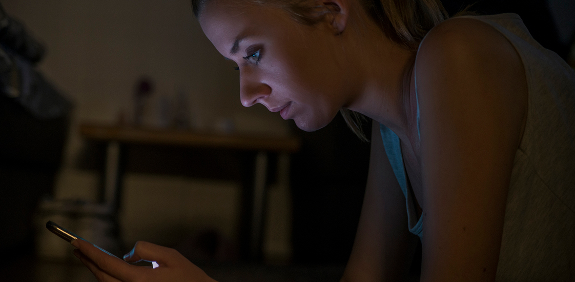 Woman sitting in the dark looking at her phone