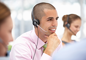 Man wearing a phone headset; woman wearing a similar headset in the background