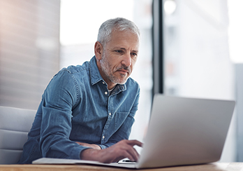 Older man sitting at a table, looking at a laptop