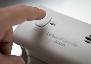 A finger about to depress the test button on a carbon monoxide detector