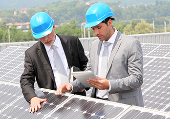 Two men in suits and hardhats consulting plans and looking at solar panels