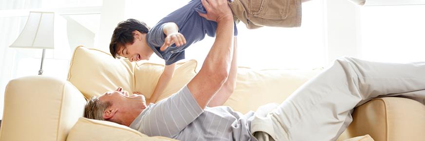 Parent lying down on the couch, holding a child up in the air