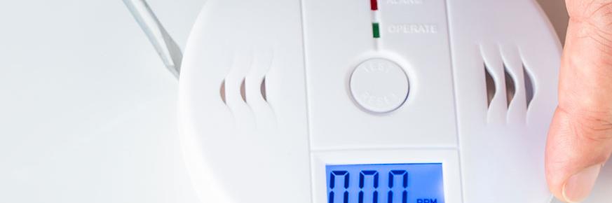 Man adjusting carbon monoxide detector and explaining the symptoms of CO2 poisoning so you can answer the question what is carbon monoxide.