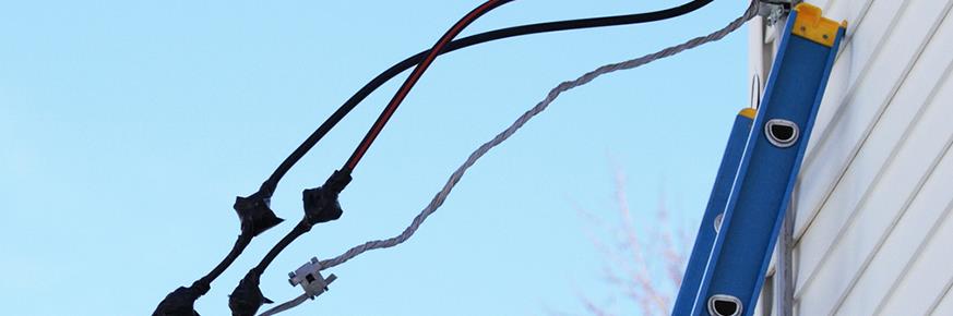 A ladder leaning against a house that has an unsafe installation of wires sticking out the side