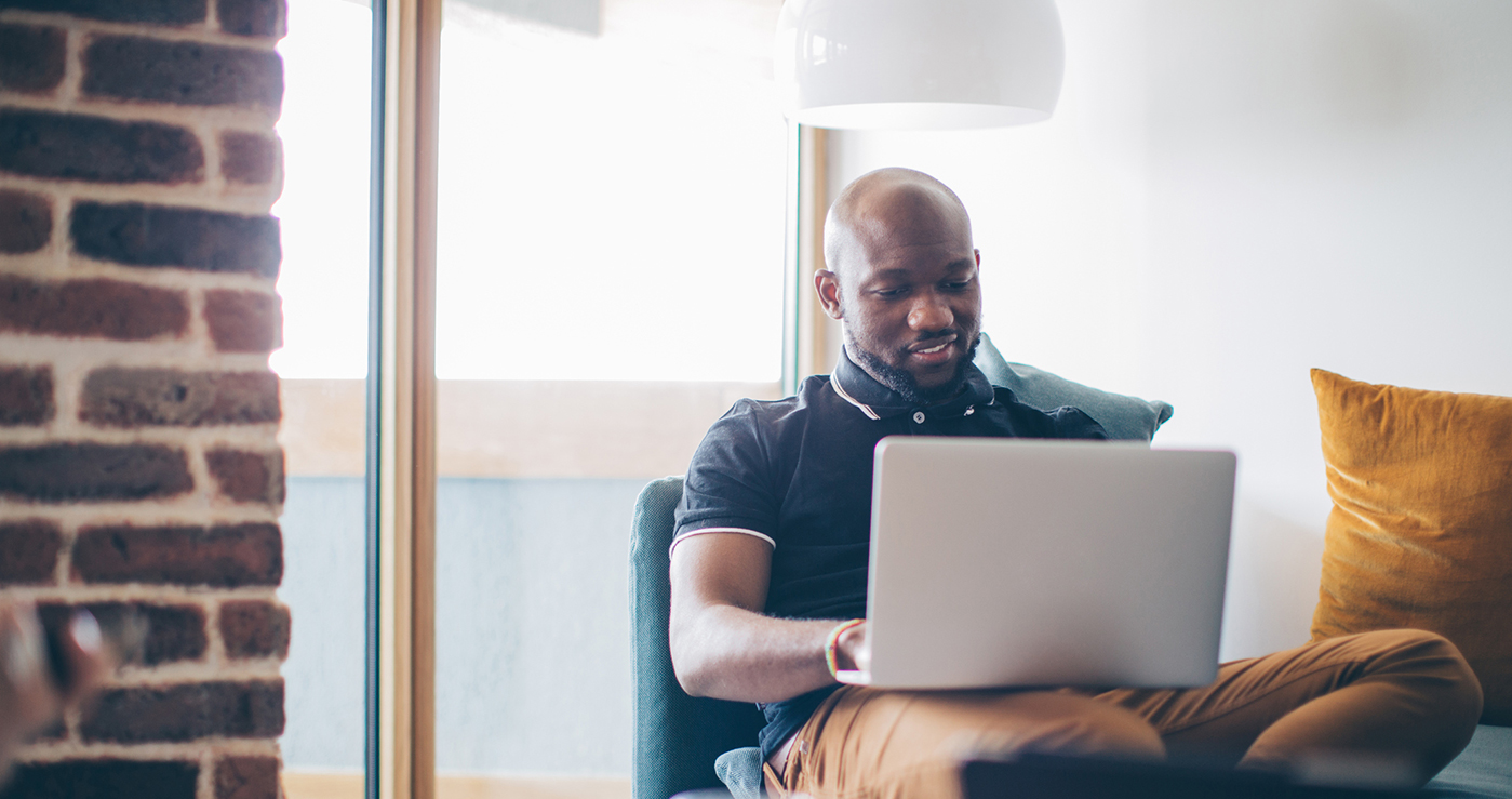 Man sitting at home on a sofa working on a laptop.